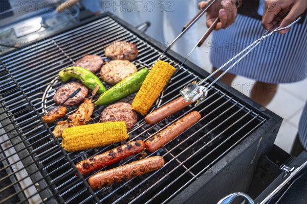 Chefs grilling several hot dogs, hamburgers, corn and peppers on a hot grill for a summer barbecue party