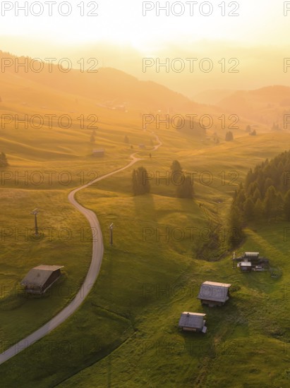 Undulating hills and forests in sunset mood with scattered mountain huts, Alpe di Siusi, Dolomites, South Tyrol, Italy