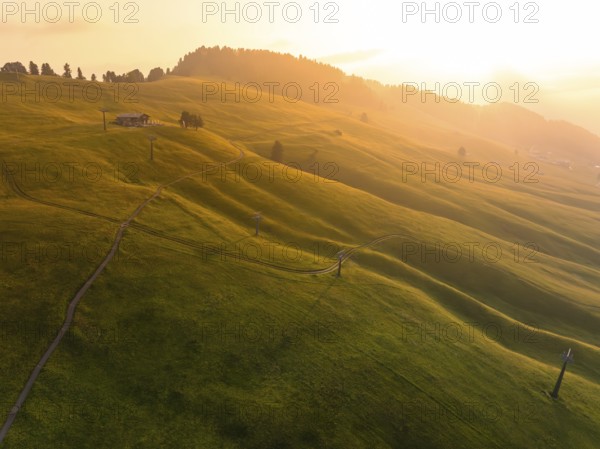 Green, gentle hills in warm light with paths and a secluded building, Alpe di Siusi, Dolomites, South Tyrol, Italy