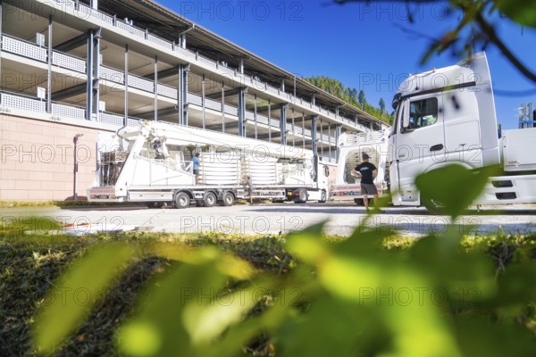 Lorry and trailer in front of a modern building, surrounded by green leaves in the foreground, Ferris wheel construction, Calw, Germany