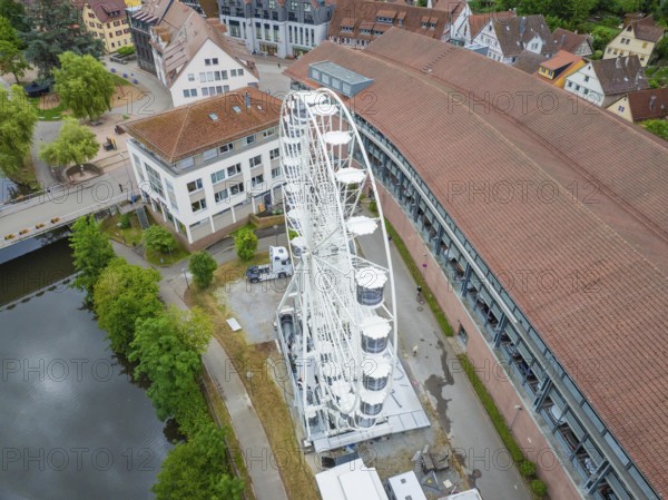 A large white Ferris wheel stands next to modern buildings with red roofs in an urban setting, Ferris wheel construction, Calw, Black Forest, Germany