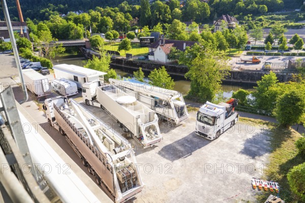 Several trucks and trailers on a car park, surrounded by green landscape and a river, Ferris wheel construction, Calw, Germany