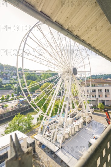 A Ferris wheel is set up in a town next to a river, surrounded by green landscape and buildings, Ferris wheel construction, Calw, Black Forest, Germany