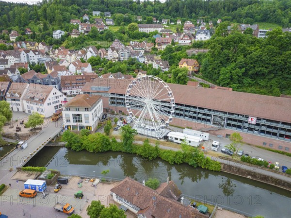 A Ferris wheel next to a river in the centre of a town with a green hilly landscape in the background, Ferris wheel construction, Calw, Black Forest, Germany