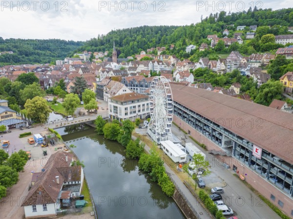 An extensive urban landscape with a central Ferris wheel, surrounded by classic house roofs and green hills, Ferris wheel construction, Calw, Black Forest, Germany