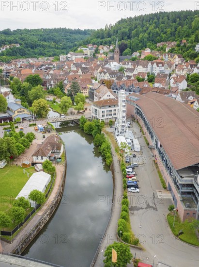 A river flows through a town with a Ferris wheel, surrounded by historic buildings and green hills, Ferris wheel construction, Calw, Black Forest, Germany