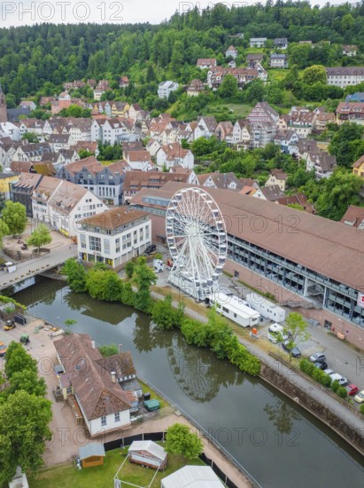 Aerial view of an idyllic village with a Ferris wheel by the river and surrounded by green hills, construction of Ferris wheel, Calw, Black Forest, Germany