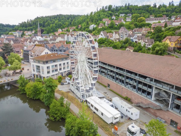 A Ferris wheel next to urban buildings embedded in a summer landscape with wooded hills, Ferris wheel construction, Calw, Black Forest, Germany