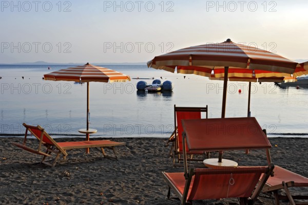 Beach, deckchairs, sunshades at the lido, Lake Bolsena, Lago di Bolsena, volcanic crater lake, calm smooth water surface, warm evening light, Bolsena, Province of Viterbo, Lazio, Italy