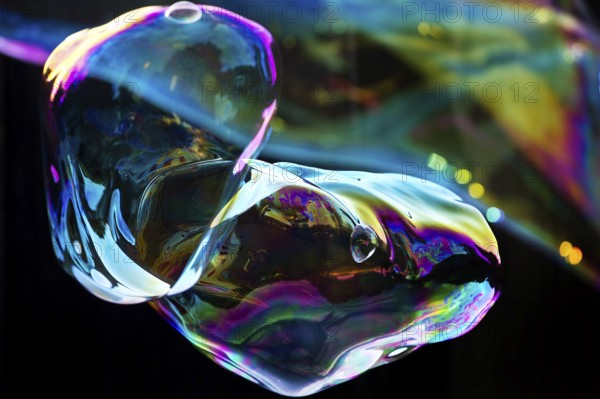 Irregular, iridescent soap bubble in the colours of the rainbow against a black background, Recklinghausen, Germany