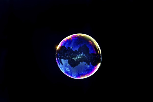 A shimmering and floating soap bubble in the colours of the rainbow against a black background, Recklinghausen, Germany
