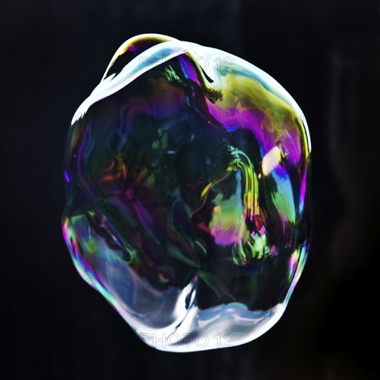 A large iridescent and floating soap bubble in the colours of the rainbow against a black background, Recklinghausen, Germany