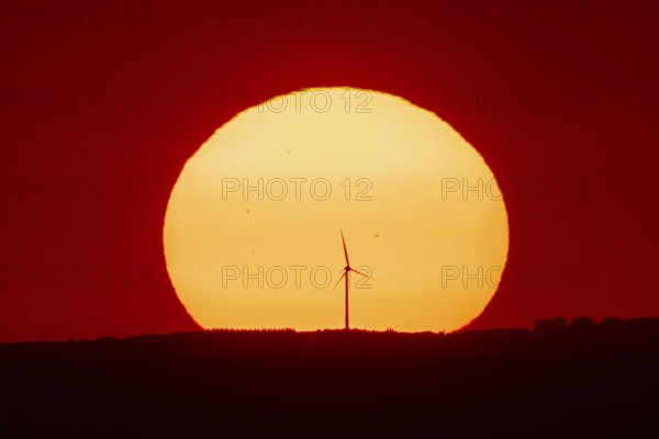 From the summit plateau of the Großer Feldberg in the Taunus mountains, you can watch the sun set behind a wind turbine on the distant horizon, Hesse, Germany