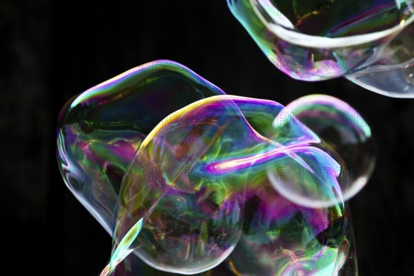 Large, irregular, iridescent soap bubbles in the colours of the rainbow against a black background, Recklinghausen, Germany