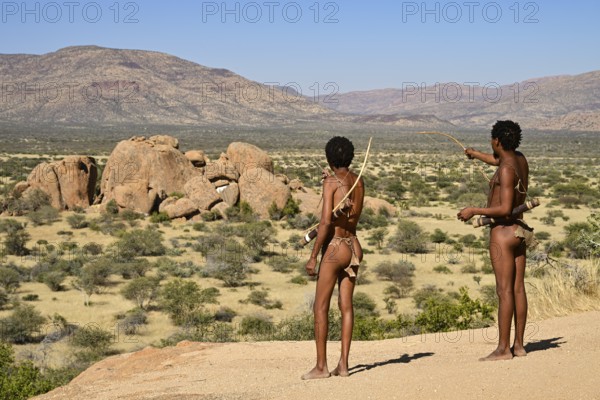 Two Bushmen with bows and arrows overlooking the landscape from a rocky hill, Erongo Mountains, Namibia