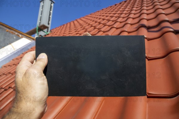 Man holding a sign with space for text in front of a recently tiled roof