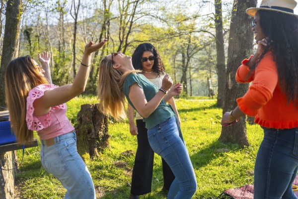 Four friends enjoying a sunny day in the park, dancing and listening to music from a portable speaker
