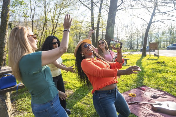 Four multi ethnic women dancing and having fun in a park, one of them is filming with her phone
