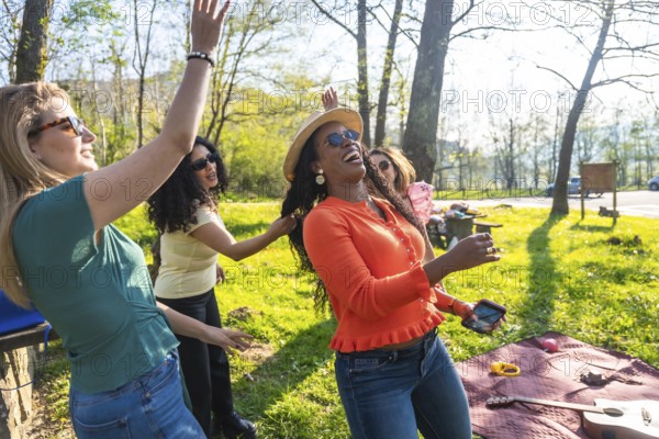 Four women dancing and enjoying themselves during a picnic in a park, celebrating friendship and leisure time
