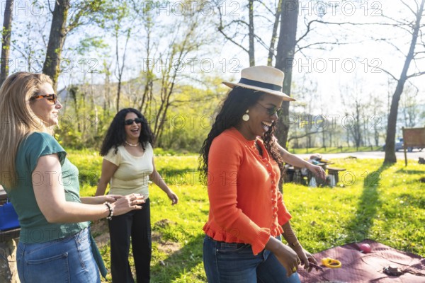 Three female friends enjoying a picnic in a park, playing and laughing together on a beautiful sunny day