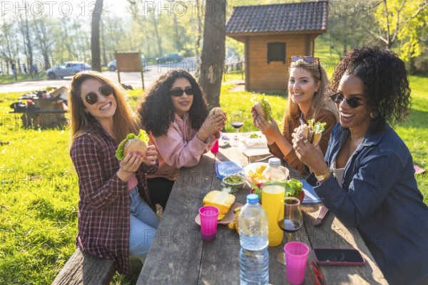Four female friends enjoying a picnic lunch together, eating sandwiches and sharing good times outdoors
