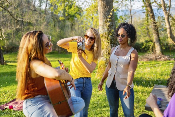 Group of friends soaking up the sun in nature, playing music, capturing moments with cameras, and enjoying each other's company