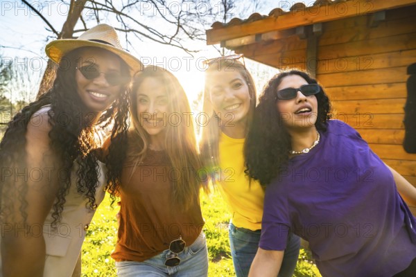 Four diverse young women are smiling and embracing outdoors, enjoying the warm glow of sunset light and celebrating their friendship