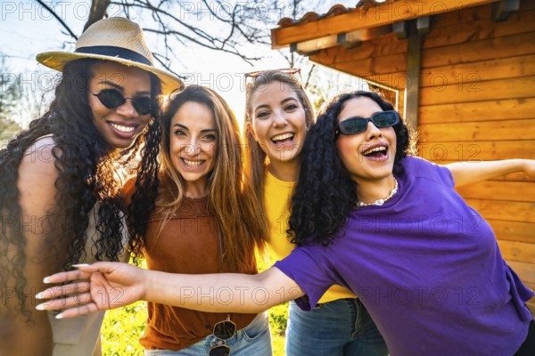 Four multi ethnic female friends are enjoying a sunny day in a garden, smiling and embracing each other