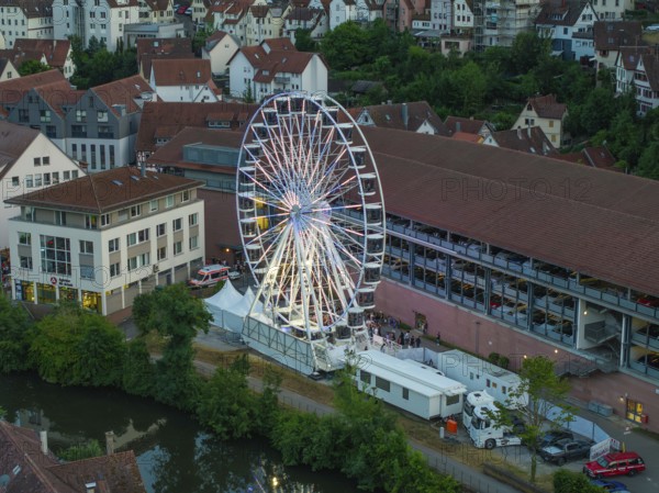 Illuminated Ferris wheel on an evening, surrounded by buildings and water, 950 years of Calw, Germany