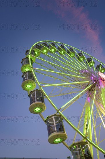 An illuminated Ferris wheel with green-red light is reflected in a river at dusk, 950 years Calw, Germany