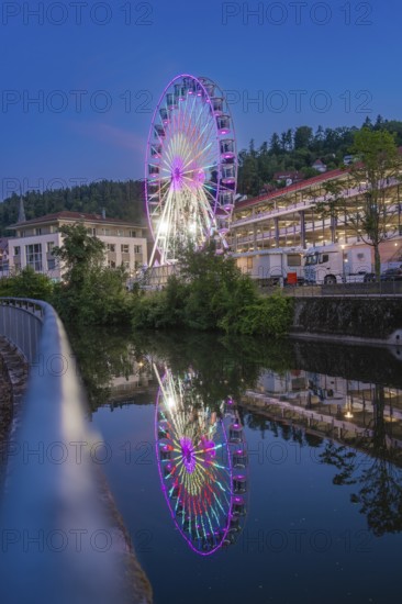 A large white Ferris wheel in front of a mountainous landscape and bright daylight, surrounded by trees and buildings, 950 years of Calw, Germany