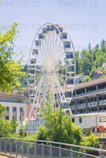A white Ferris wheel in daylight against a backdrop of buildings and wooded hills, 950 years of Calw, Germany