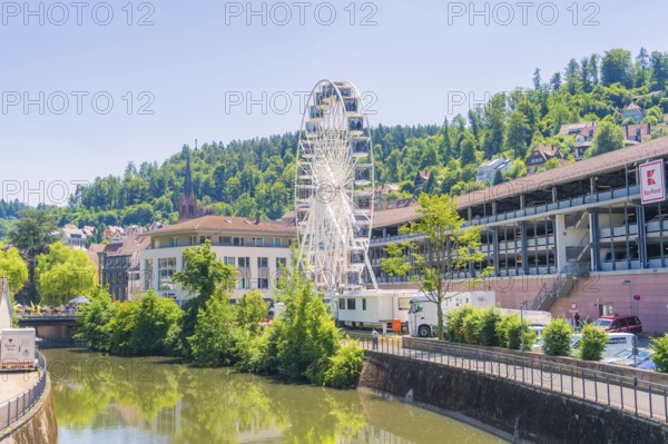 A white Ferris wheel against an urban backdrop and a green, wooded hill in bright sunlight, 950 years of Calw, Germany