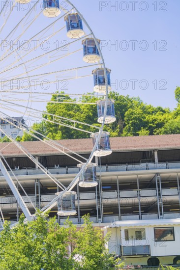 A large Ferris wheel towers over a building, surrounded by green trees under a clear blue sky, 950 years Calw, Germany