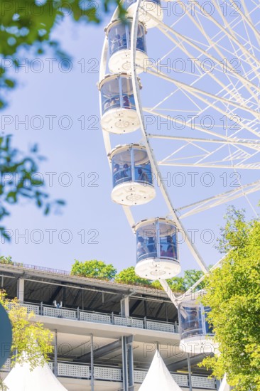 The Ferris wheel with glass cabins rises next to a large building surrounded by sunny trees, 950 years Calw, Germany