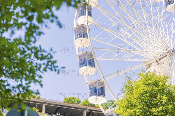 Close-up of a Ferris wheel with cabins, visible between green trees and a blue sky, 950 years Calw, Germany