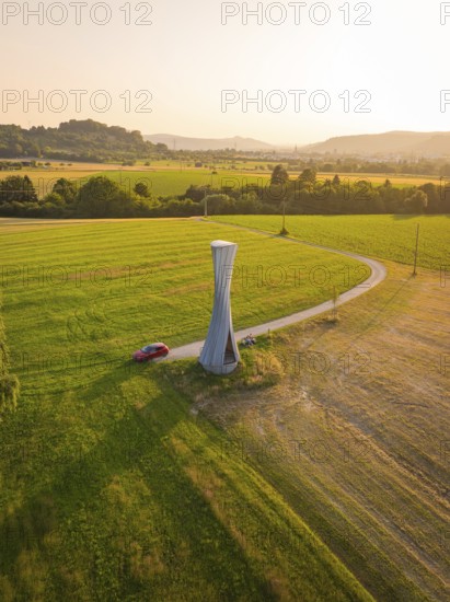 A modern observation tower in a rural setting with forests and fields at sunset