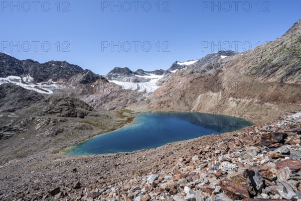 Mountaineer on hiking trail, view of blue glacial lake in rocky mountain landscape, behind Königshofspitz, Schwarzwandspitz and glacier Übeltalferner, descent from summit Roter Grat, Stubai Alps, South Tyrol, Italy