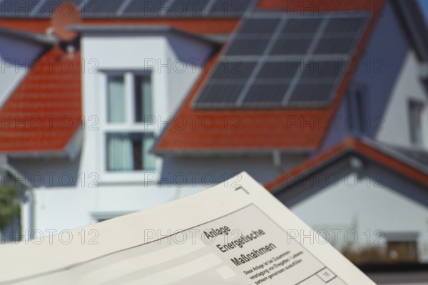 Close-up of tax return, energy measures attachment, in the background a picture of a solar roof on the screen of a laptop
