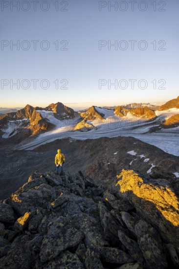 Mountaineers in front of a picturesque high mountain landscape at sunrise with alpenglow, glacier and rocky mountain peaks in the morning light, view at the Becher on mountain peak Königshofspitz and glacier Übeltalferner, Stubai Alps, South Tyrol, Italy