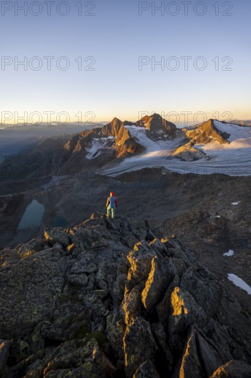 Mountaineer in front of picturesque high mountain landscape at sunrise with alpenglow, glacier and rocky mountain peaks in the morning light, view at the cup on mountain peak Königshofspitz and glacier Übeltalferner, Stubai Alps, South Tyrol, Italy