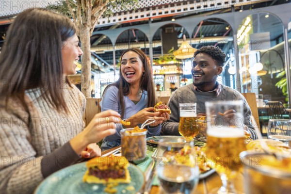 Cheerful multi ethnic friends enjoying burgers and beer, laughing and talking at a restaurant table