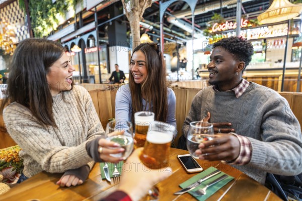 Group of cheerful multi ethnic friends toasting with beer and water at brewery pub restaurant, enjoying time together