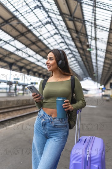 Tourist is waiting for train departure at railway station listening to music on headphones and drinking coffee
