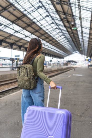 Tourist wearing headphones and carrying luggage strolls through a bustling train station, embracing the excitement of travel and adventure