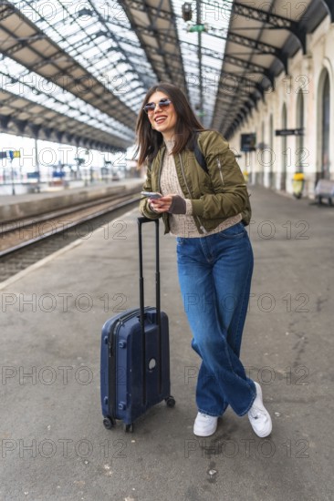 Tourist using a smartphone while waiting for the train at the railway station, enjoying the journey and planning the next destination