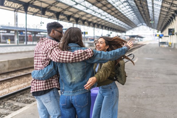 Three happy multi ethnic young adult students hug at train station after arriving for a trip together