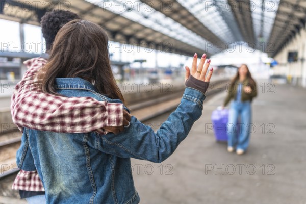 Couple waving goodbye to their friend at the train station, sharing a heartfelt moment filled with hugs and smiles before the journey begins