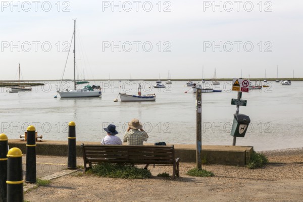 People looking out from quayside at boats moored in harbour, River Ore, Orford, Suffolk, England, UK