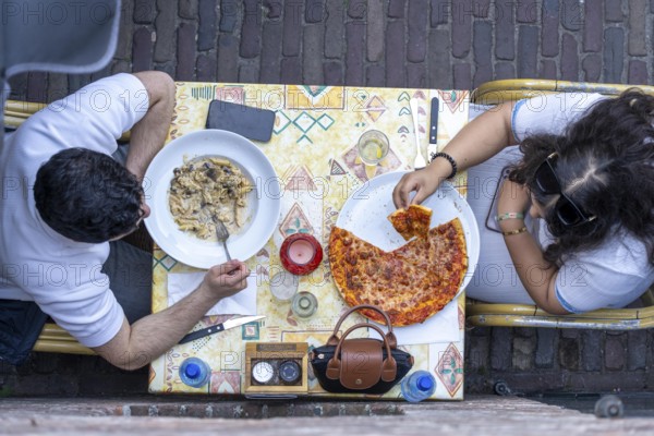 Man and woman sitting in an Italian restaurant eating pizza and pasta, symbolic picture